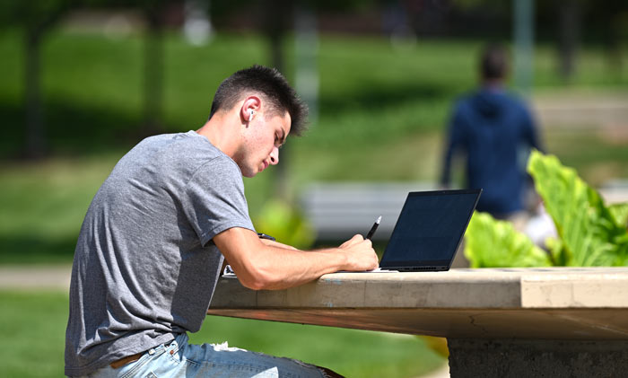 一个学生的笔记本电脑在Coleman Common户外学习的桌子上学习