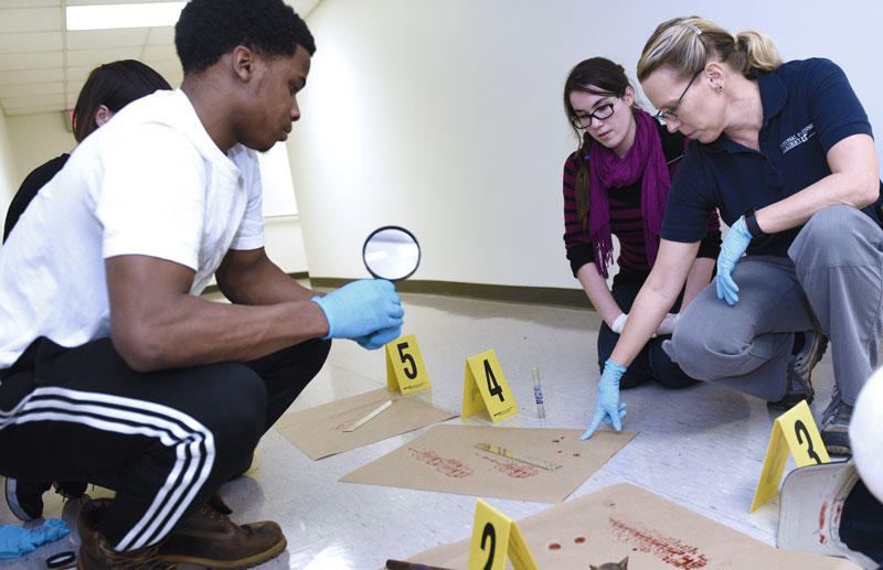 在一个法医实验室里，学生们正在观察一名教师关于虚构的犯罪现场的观点。