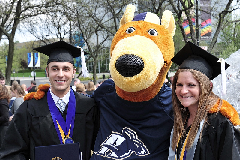 两名穿着毕业礼服的UA学生和阿克伦大学的吉祥物Zippy站在一起betway苹果